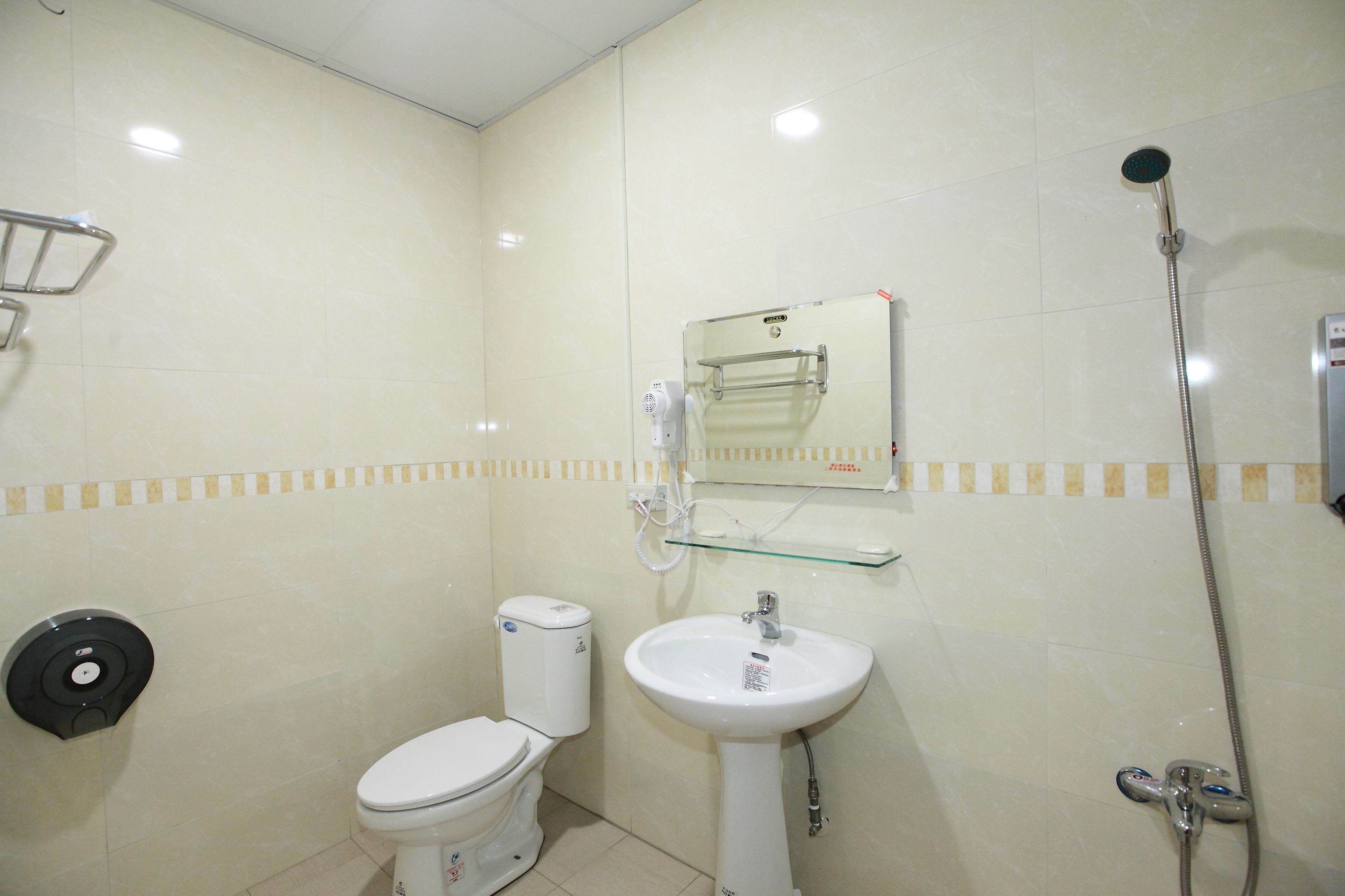 A bathroom with a toilet, a sink, a glass shelf, a shower, and a hand dryer.