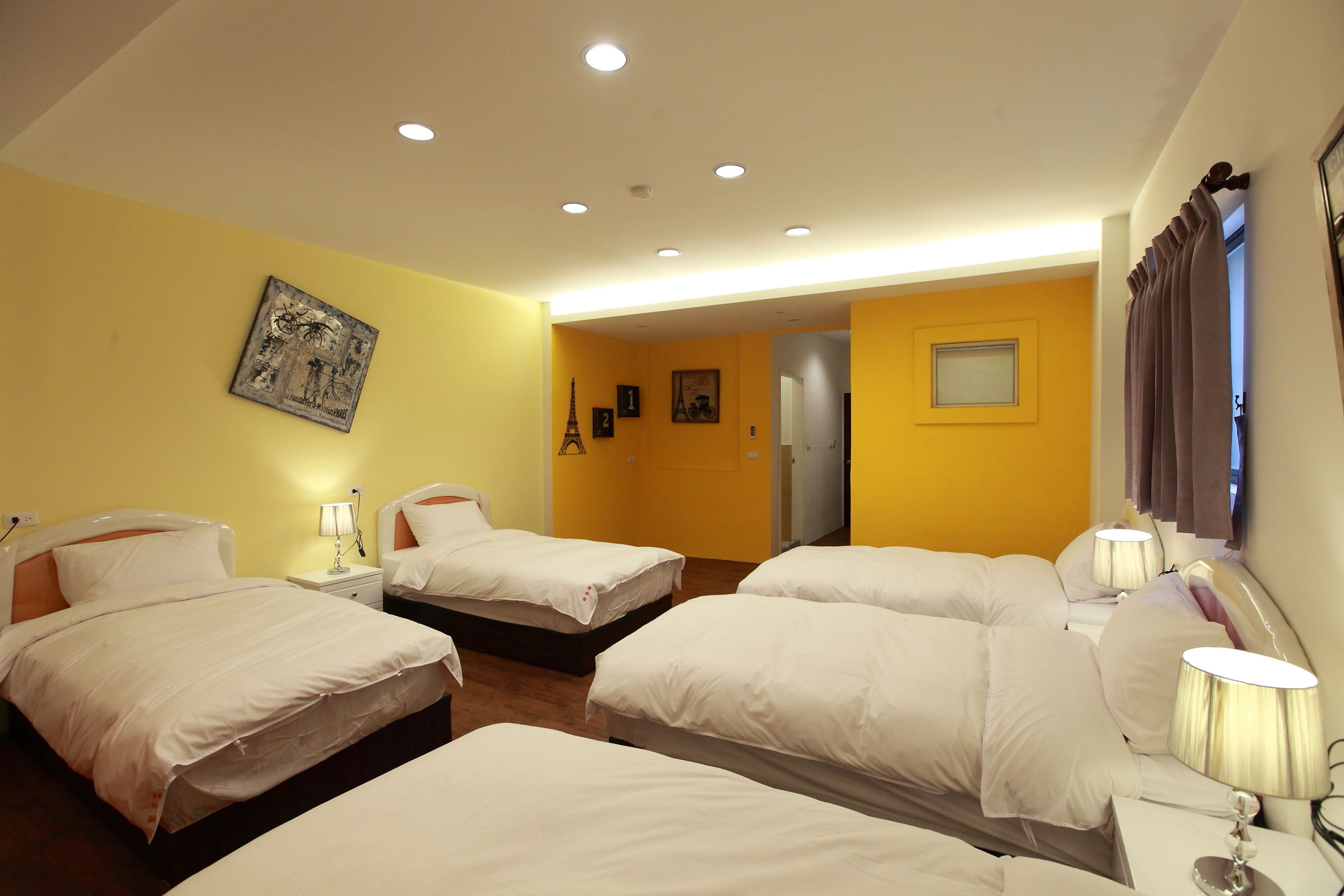 Una habitación de hotel con cuatro camas, una pared amarilla y una puerta que da a otra habitación.