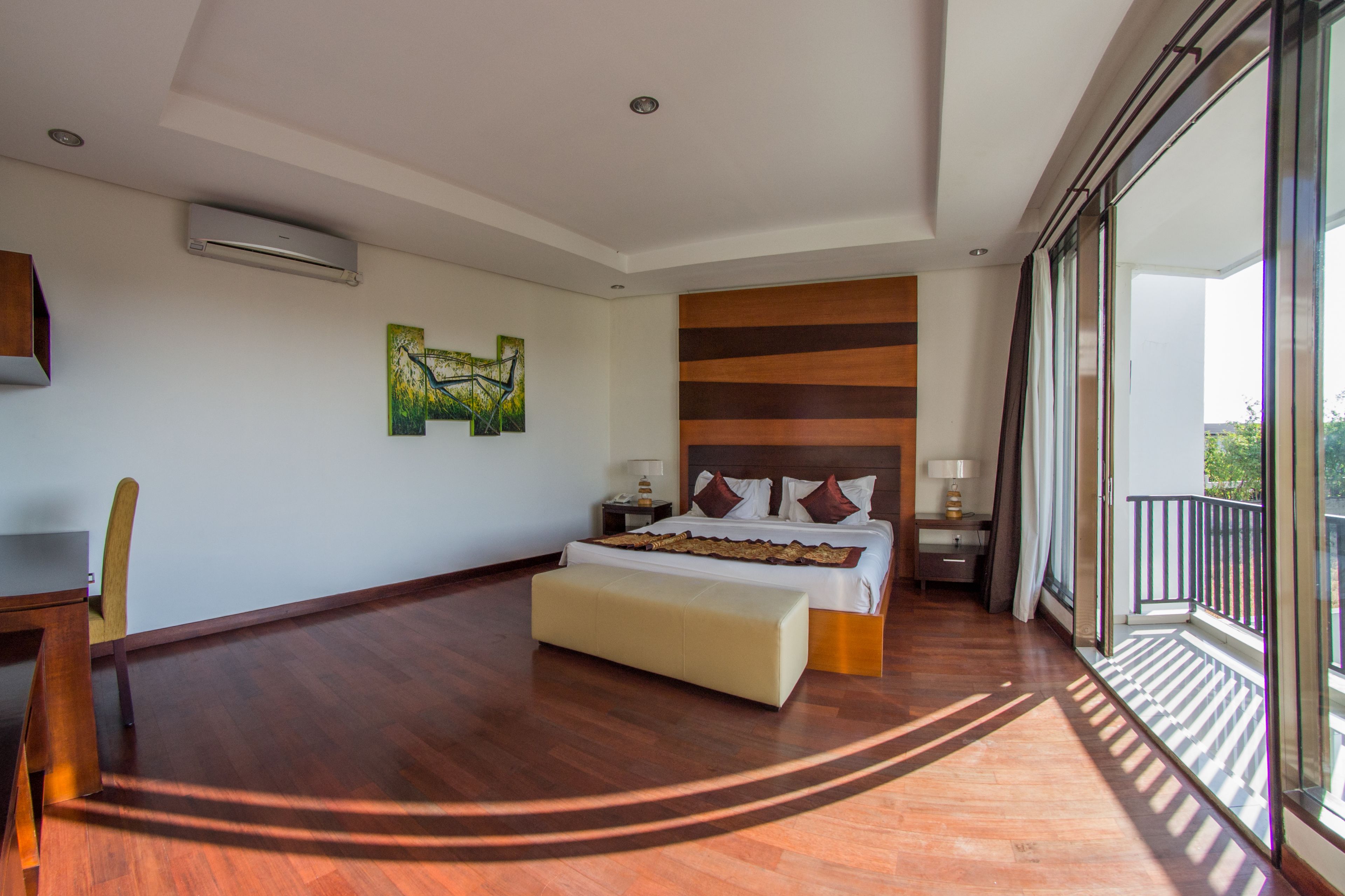 Une chambre d’hôtel spacieuse, dotée d’un grand lit, d’un plancher en bois, d’un balcon avec vue et d’un bureau avec une chaise.