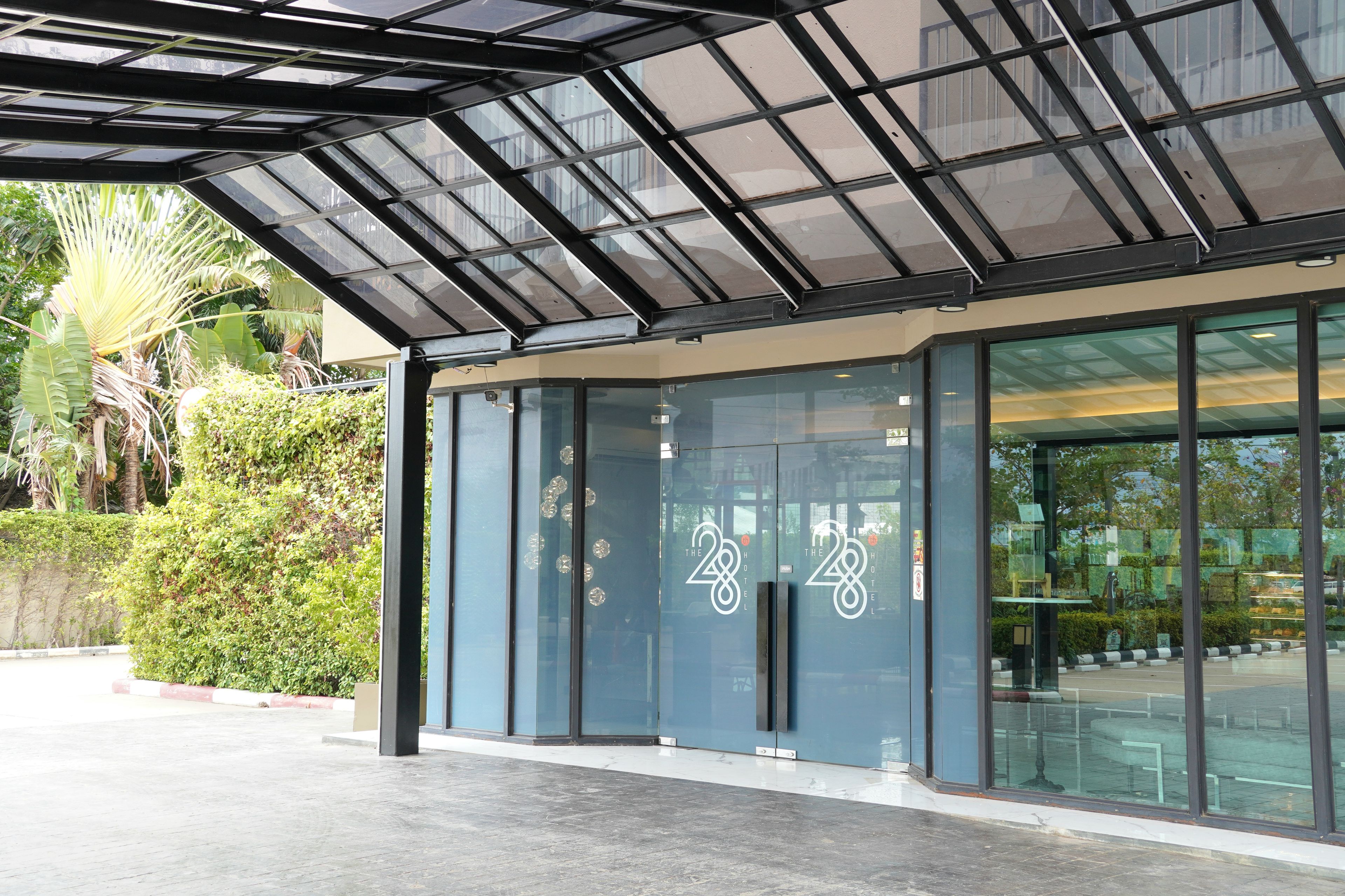 L’entrée d’un hôtel moderne, avec une façade en verre, une structure de toit en métal et un jardin bien entretenu.
