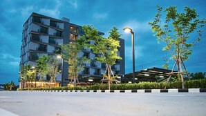 A modern multi-story building with a flat roof, surrounded by trees and street lamps. - The 28th Hotel (Kanchanaburi)