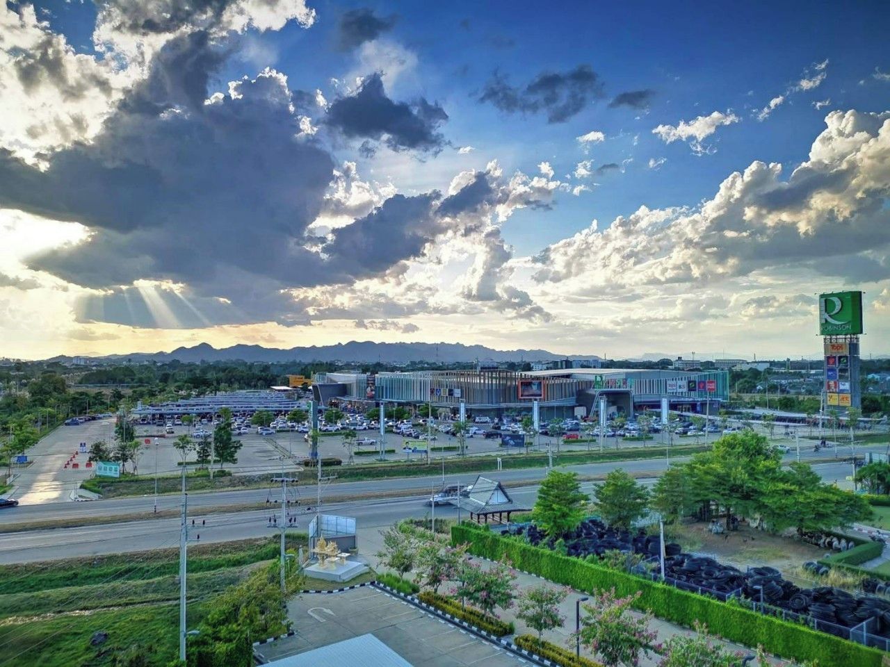 A large parking lot with multiple rows of parked cars, a building with a modern design, and a clear sky with clouds.