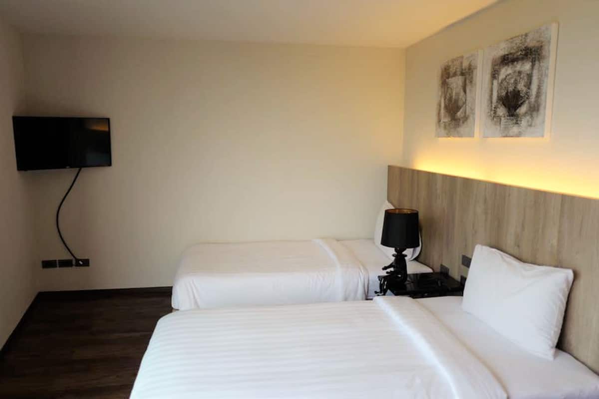 Une chambre d’hôtel avec deux lits, un téléviseur à écran plat fixé au mur et deux tableaux abstraits au-dessus des lits.