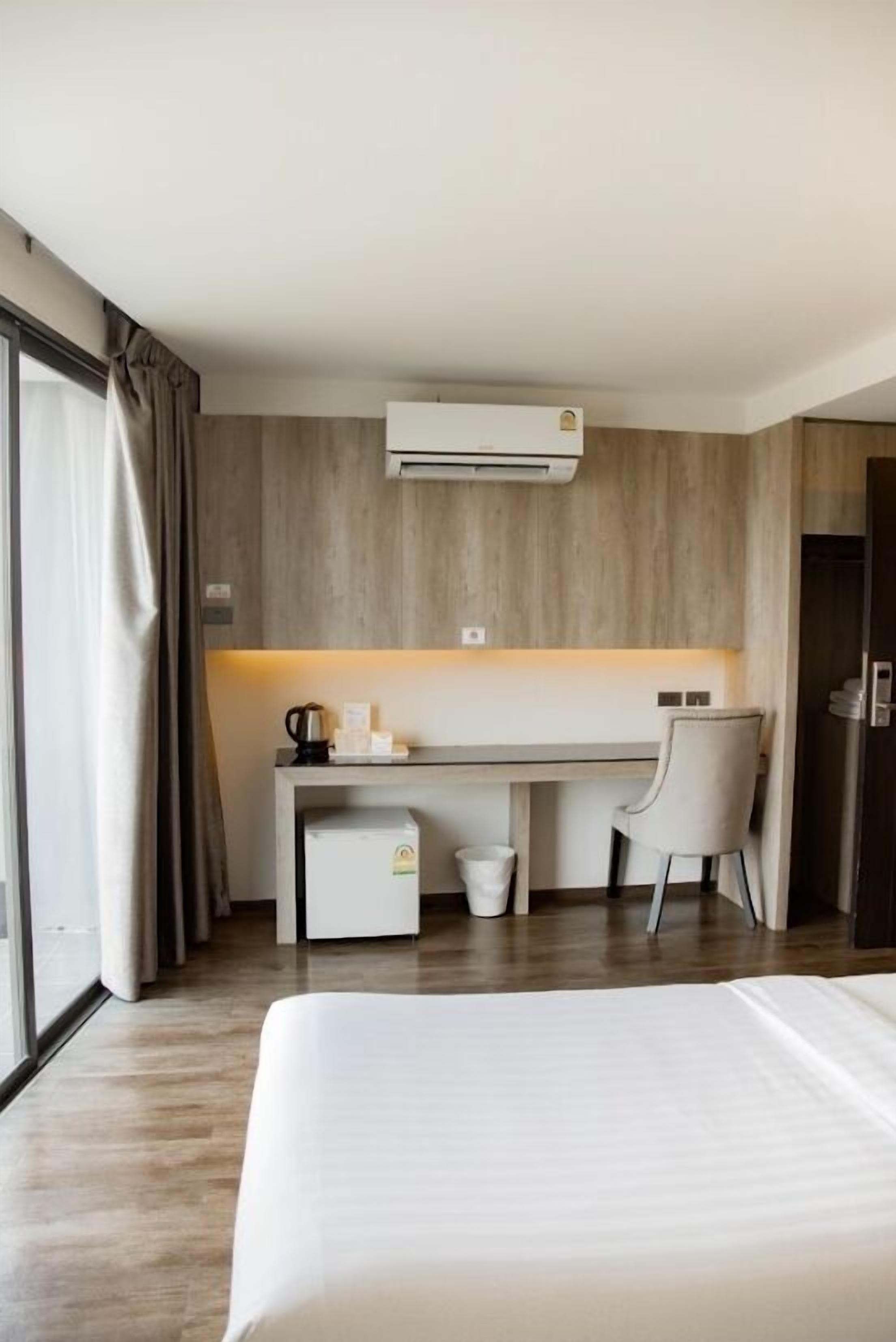 A hotel room with a bed, a desk, a chair, an air conditioning unit, and a window with curtains.