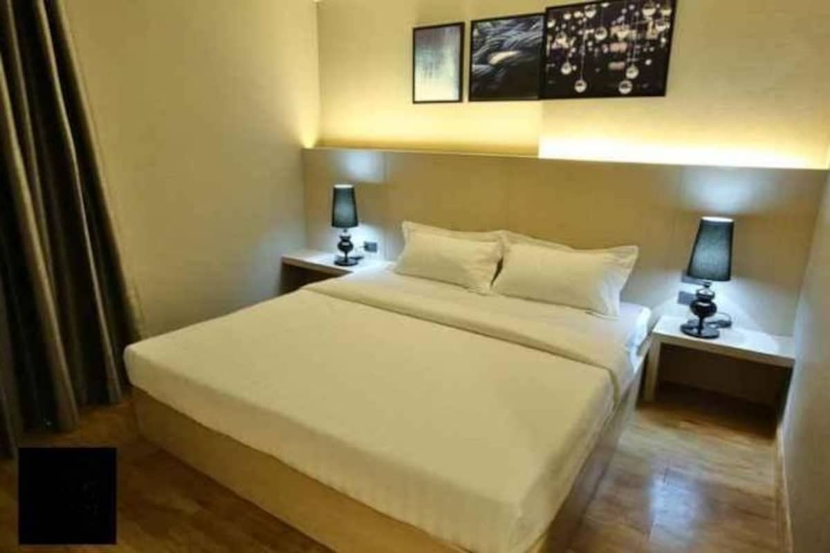 Habitación de hotel con una cama grande, dos mesitas de noche con lámparas, y una obra de arte colgada en la pared sobre la cama.
