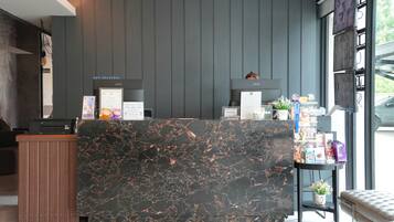A reception desk with a marble top, a wooden counter, and a grey wall with vertical lines.