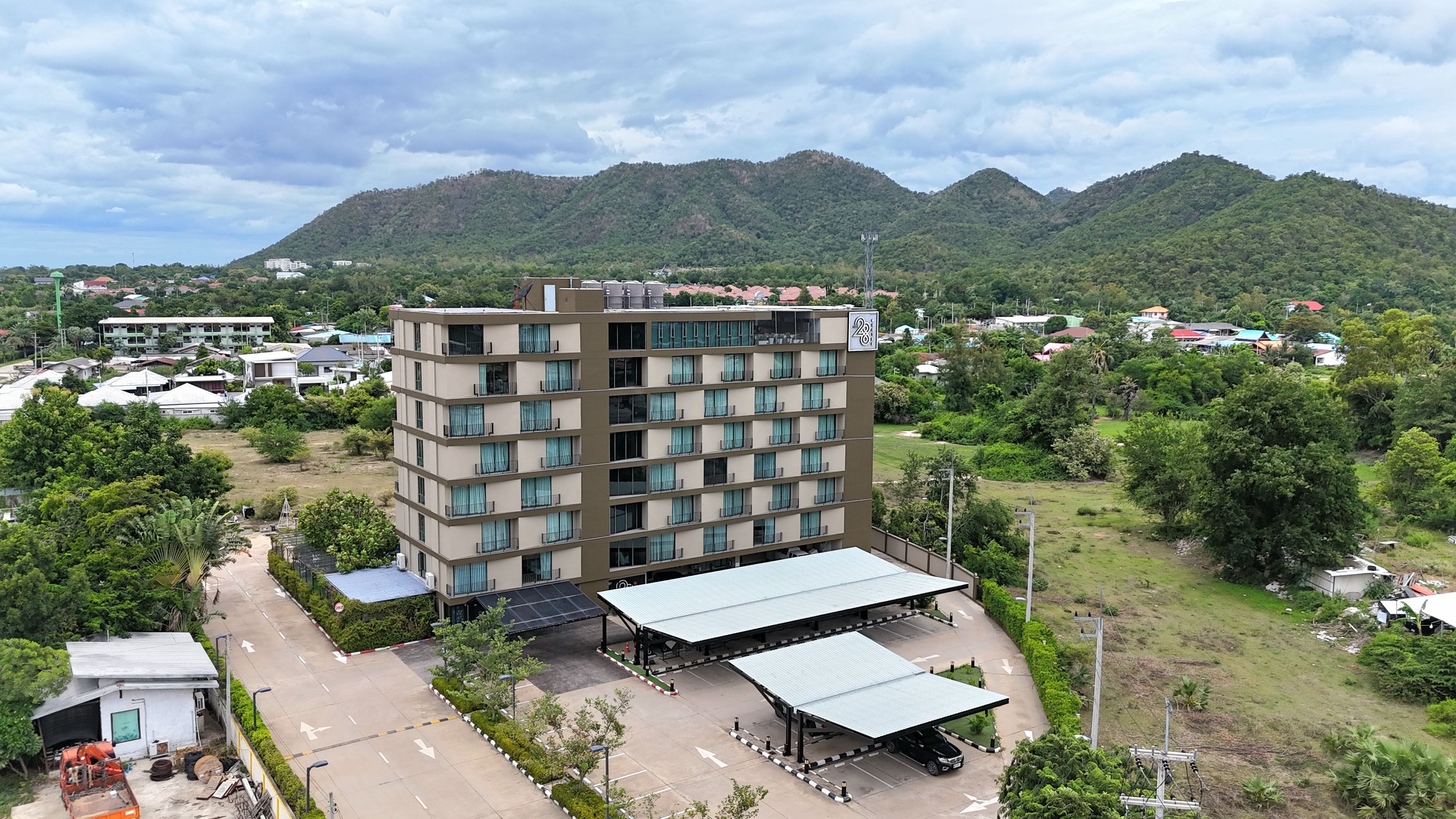 A multi-story hotel with a flat roof and balconies, surrounded by greenery and mountains.