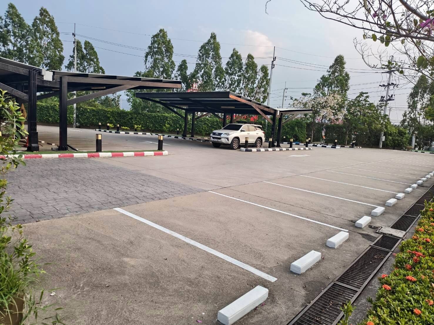 A parking area with a white car, marked parking spaces, and a covered walkway.