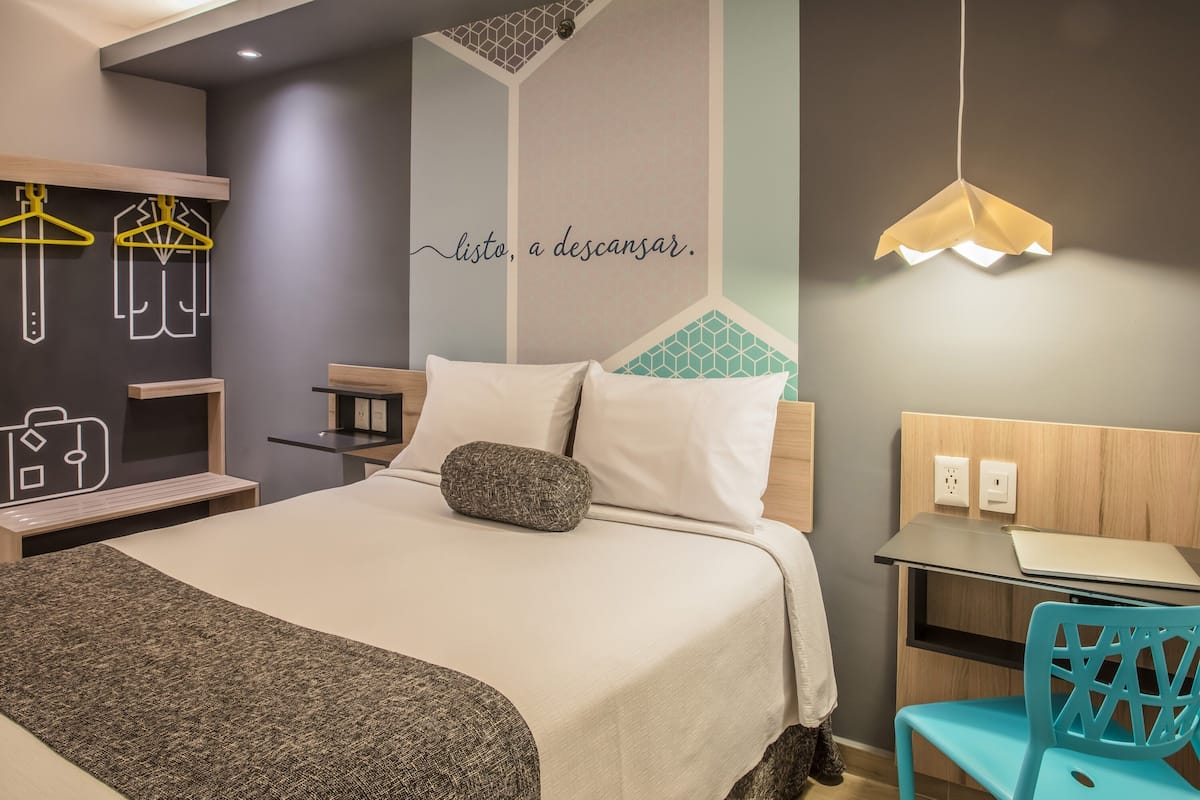 Une chambre d’hôtel moderne avec un lit bien fait, un bureau avec un ordinateur portable et une chaise.