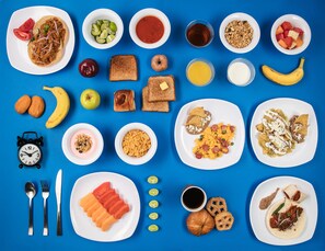 Variedad de alimentos para desayuno y frutas dispuestas en platos y tazones sobre un fondo azul.