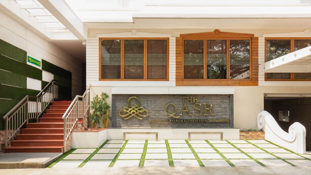 A hotel entrance with a reception desk, a staircase, and a sign indicating the name "The QASR Premium Business Hotel". - Treebo The Qasr (Kanayannur)