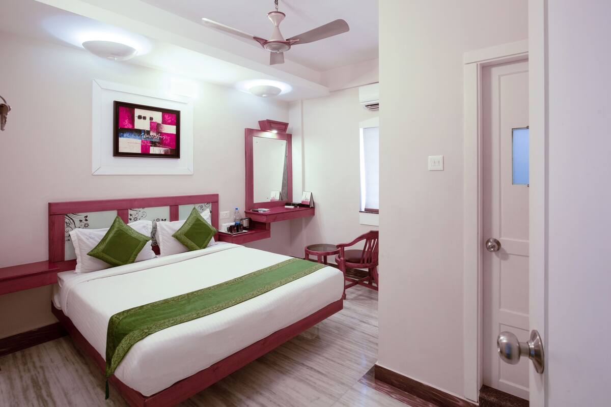 Quarto de hotel com cama, escrivaninha, cadeira, espelho e ventoinha no teto.