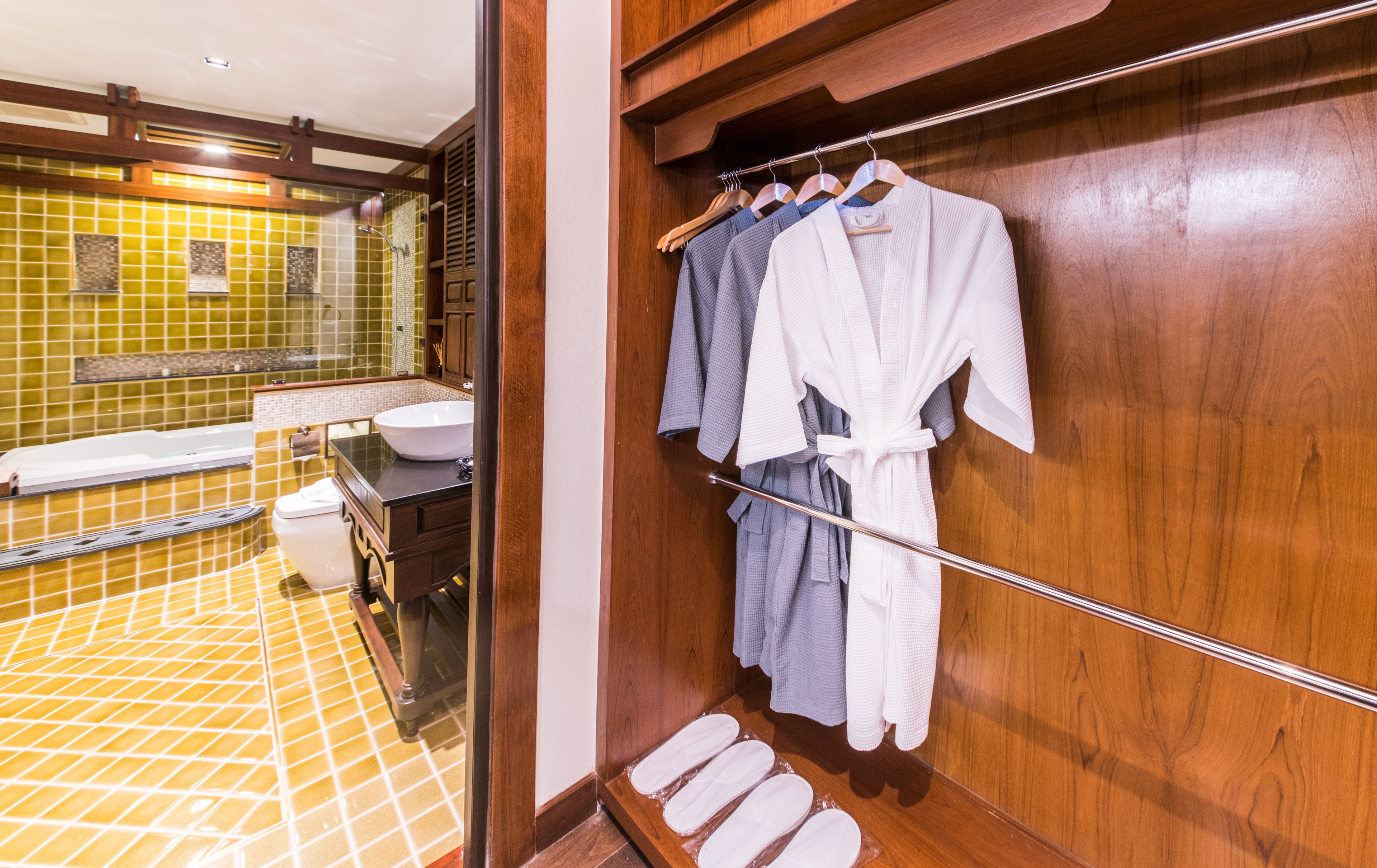A bathroom with a bathtub, a sink, and a wooden vanity. There are wooden bath mats and a towel rack with robes.