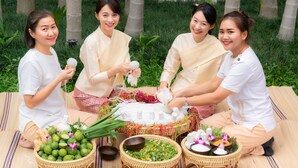 Four individuals seated on a mat outdoors, surrounded by various items including baskets of herbs and flowers, and a woven mat. - Phra Singh Village (Chiang Mai)