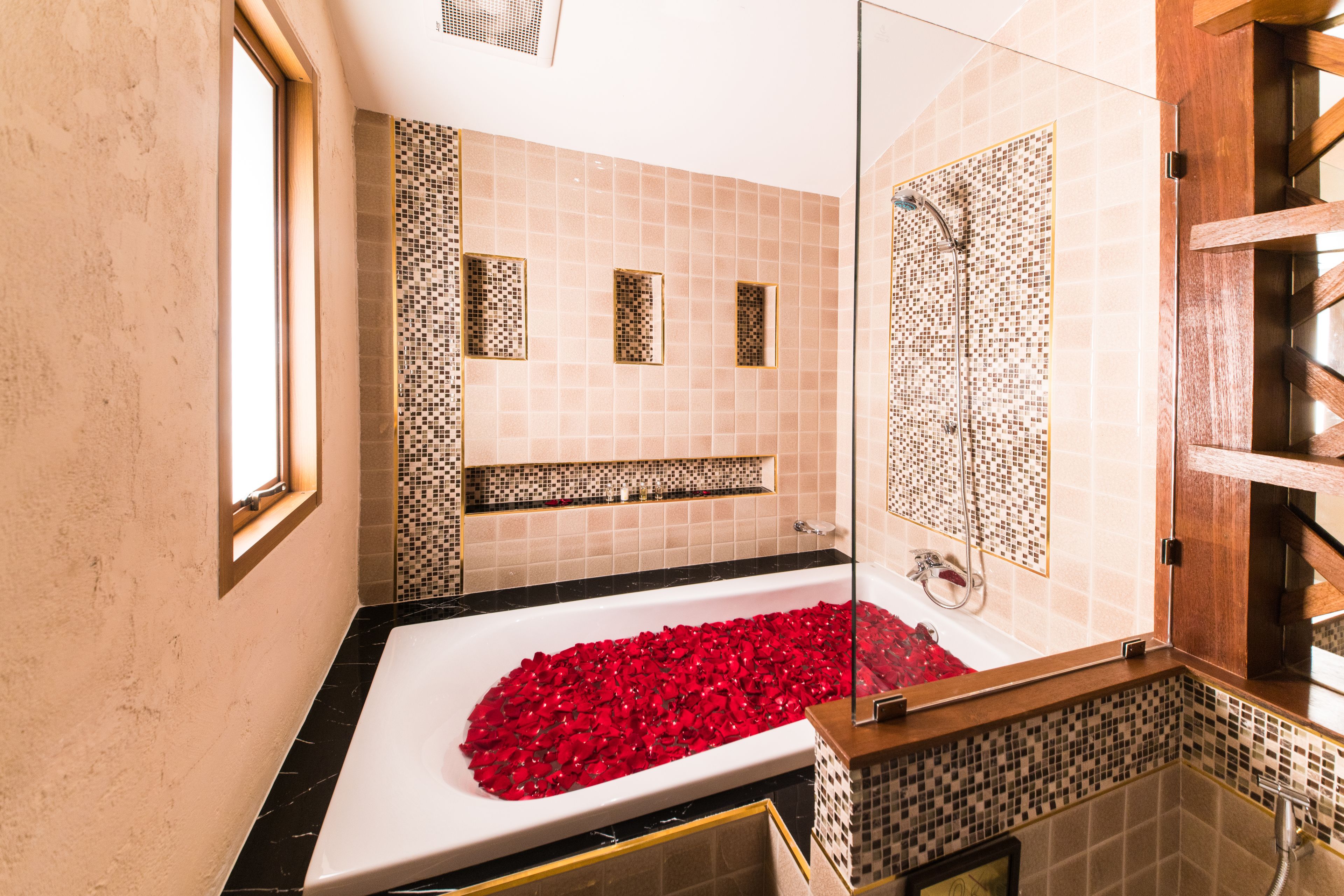 Un baño con una bañera grande llena de pétalos de rosa, un espejo y paredes de azulejos.