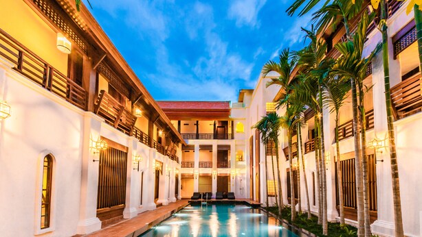 A pool area with a clear view of the pool, surrounding buildings, and palm trees. - Phra Singh Village (Chiang Mai)