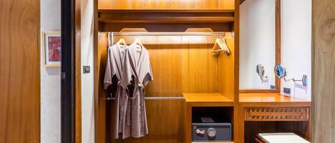 A wooden walk-in closet with hanging robes, a shoe rack, and a small table.