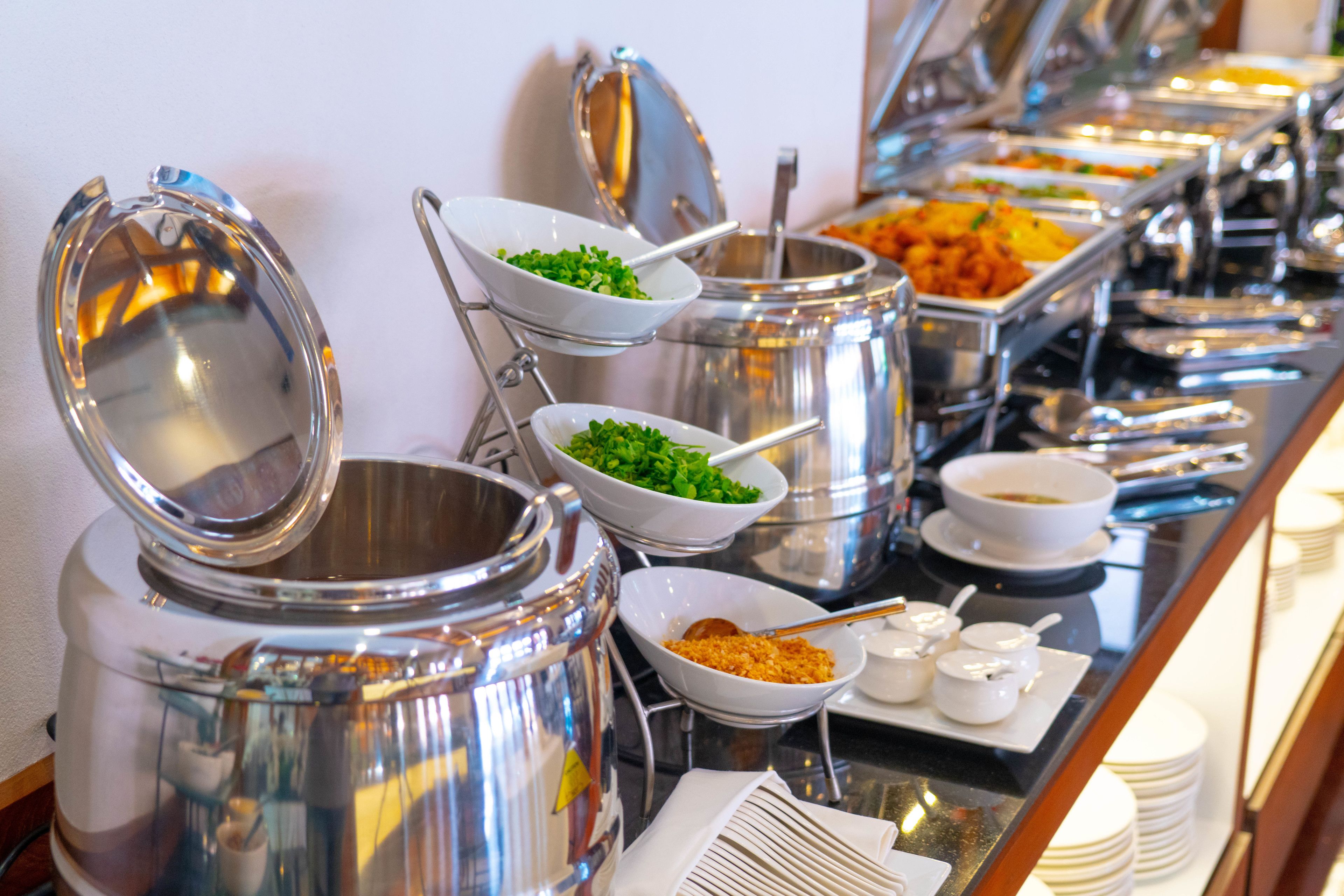 Un bufé con diversos alimentos en recipientes metálicos, incluyendo ensaladas y otros platos.