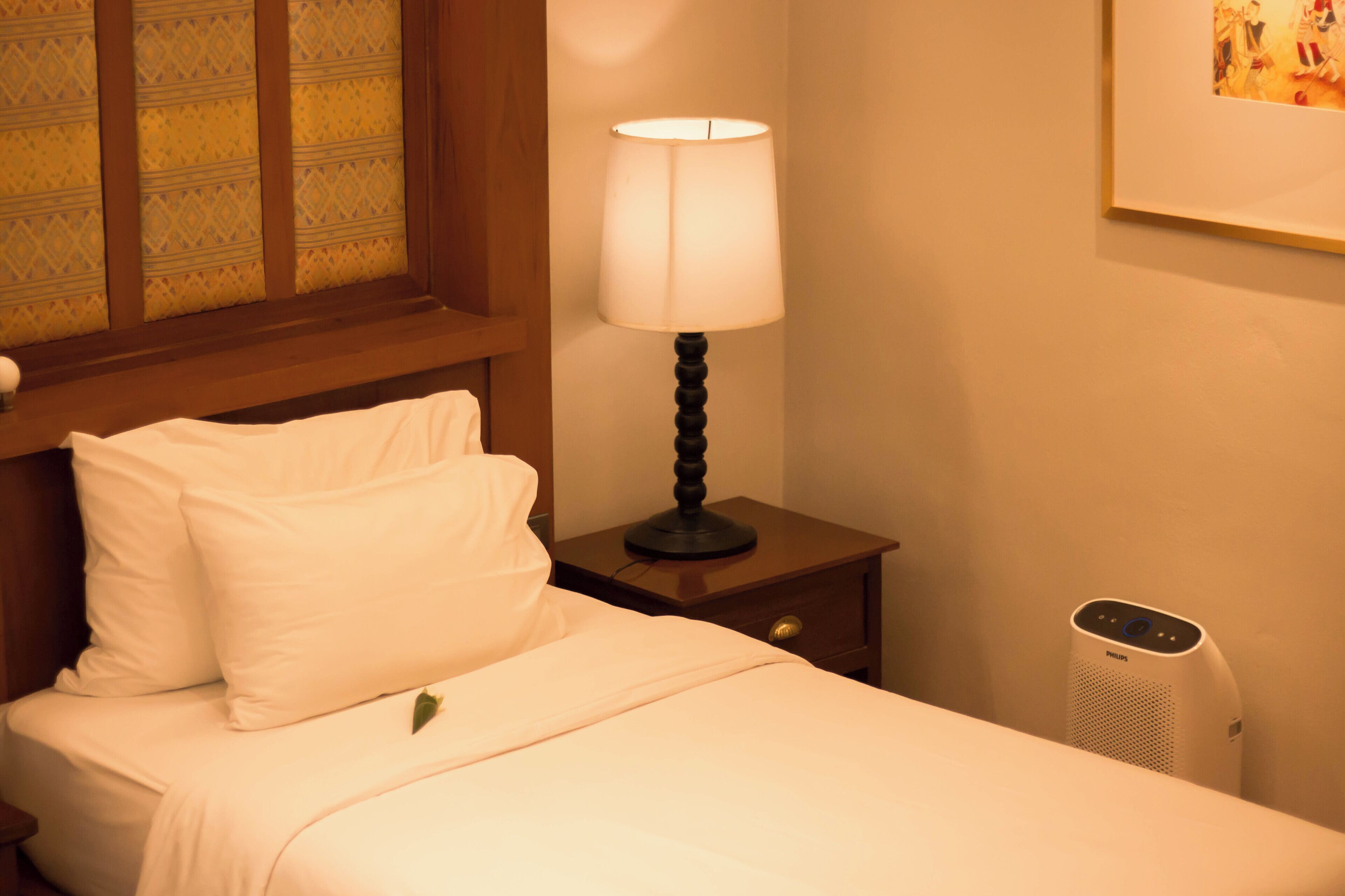 A neatly made bed with white linens, a bedside lamp, and a wall-mounted air purifier.