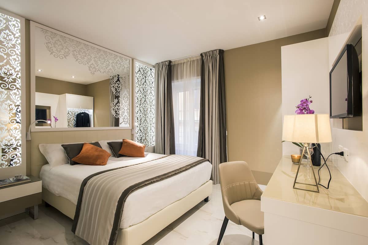 Une chambre d’hôtel comprenant un lit, un bureau, une chaise, une télévision et un miroir décoratif.
