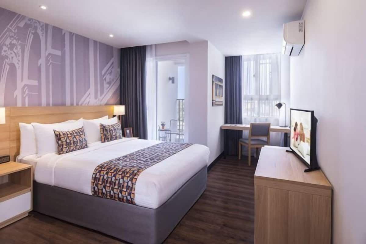 A modern hotel room with a large bed, a desk, a chair, and a TV.