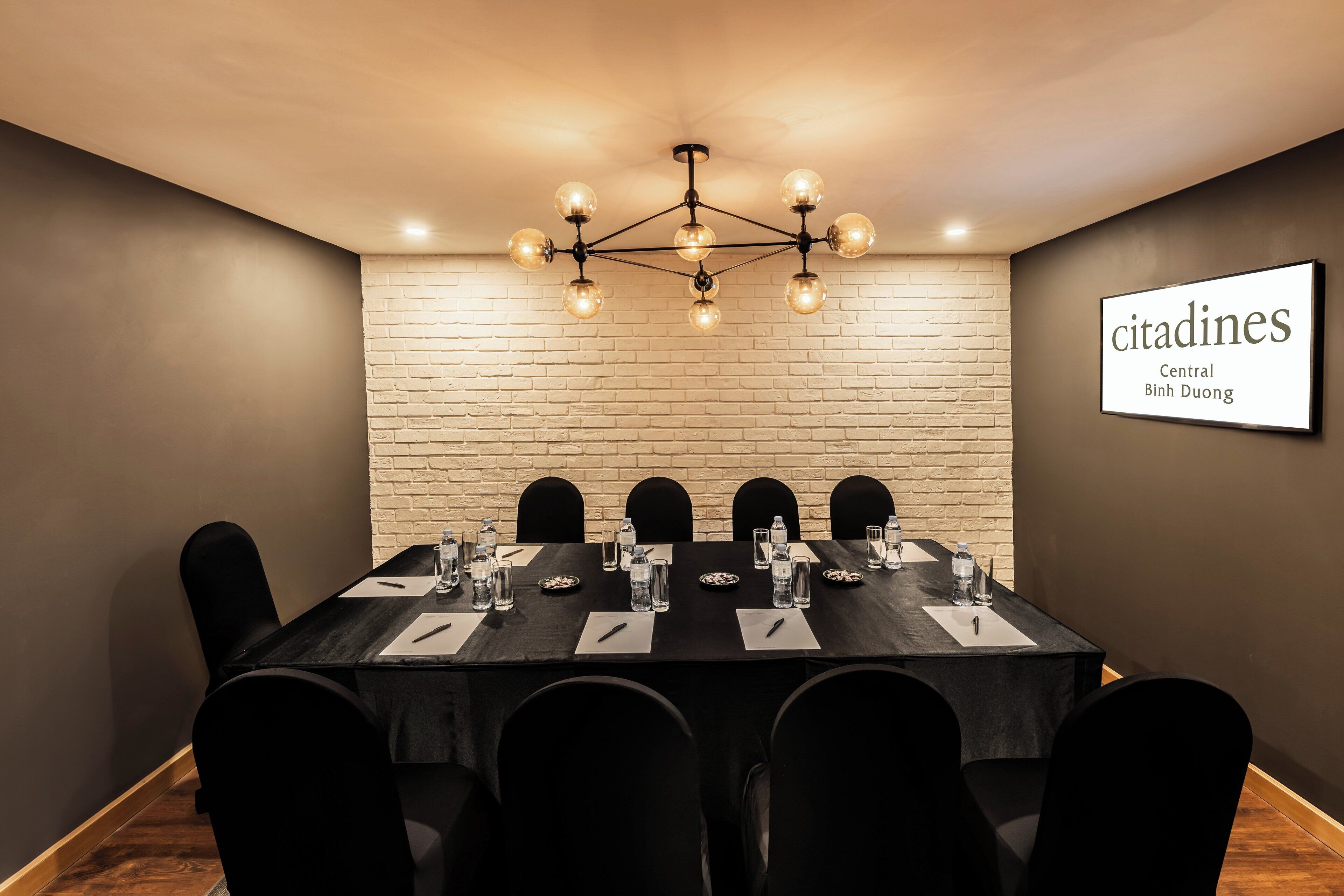 A conference room with a brick wall, a chandelier, and a sign reading "citadines Central Binh Duong".
