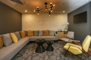 Una sala moderna con un sofá modular, dos mesas redondas para café, un sillón amarillo y una lámpara esférica original.