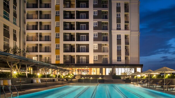 Un hotel con piscina, mobiliario exterior y un edificio grande con varios balcones.