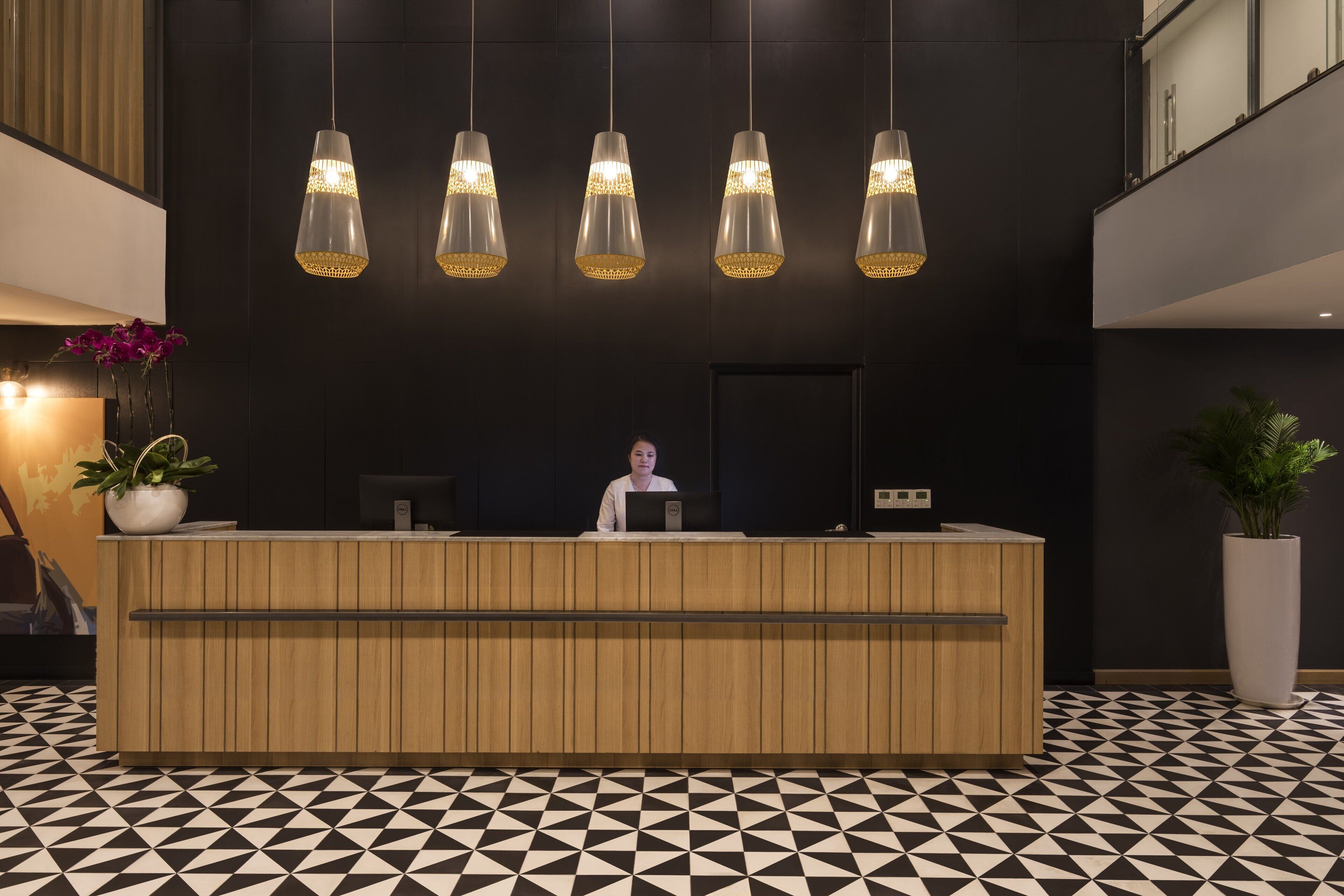 Una recepción con encimera de madera, suelo con estampado blanco y negro, y lámparas colgantes con detalles dorados.