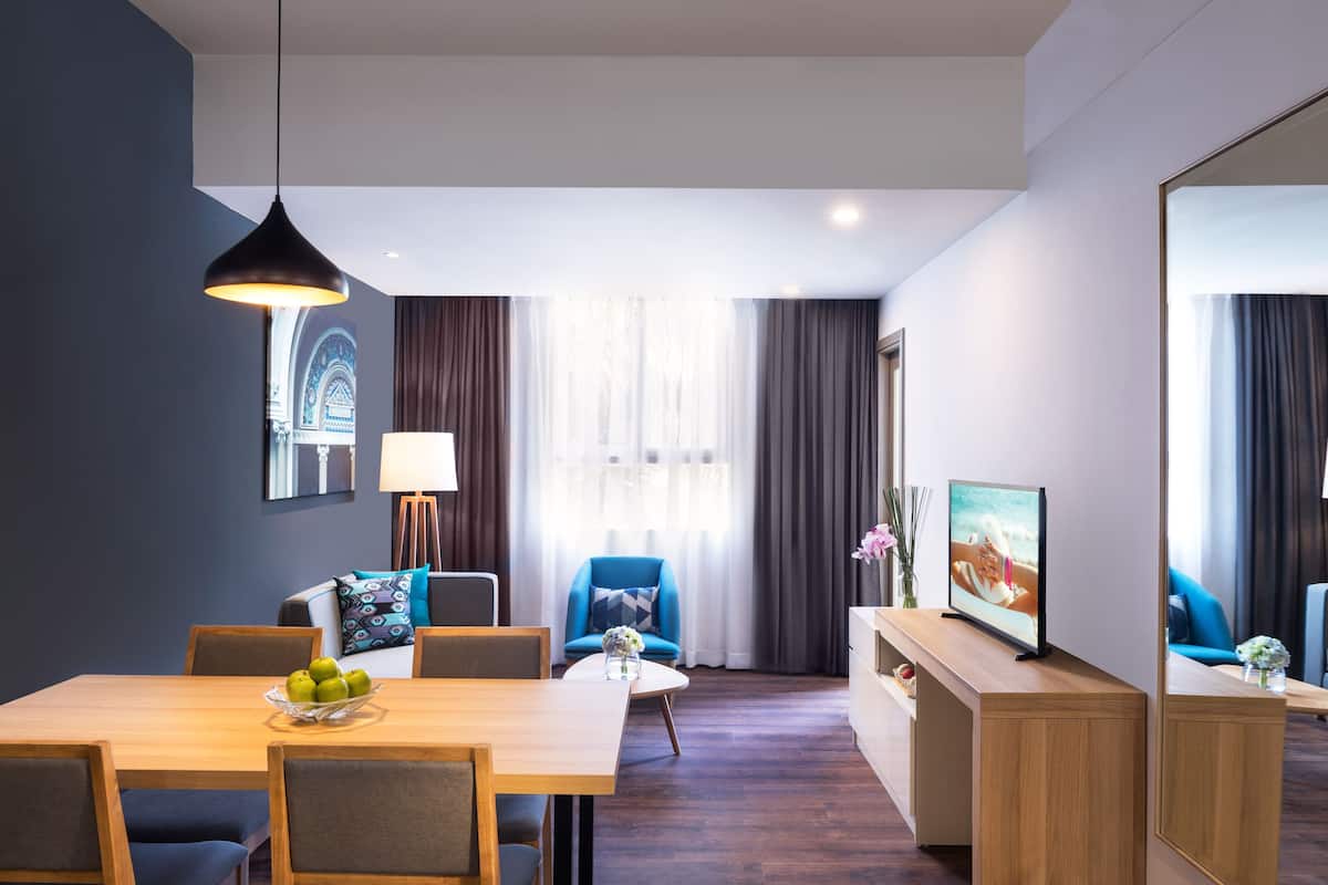 A modern hotel room with a dining area, a sofa, a TV, and a large mirror.