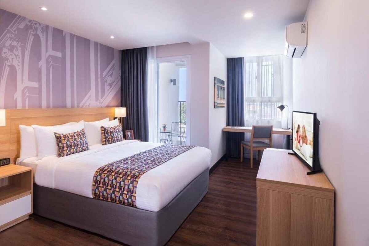 A modern hotel room with a large bed, a desk, and a balcony.