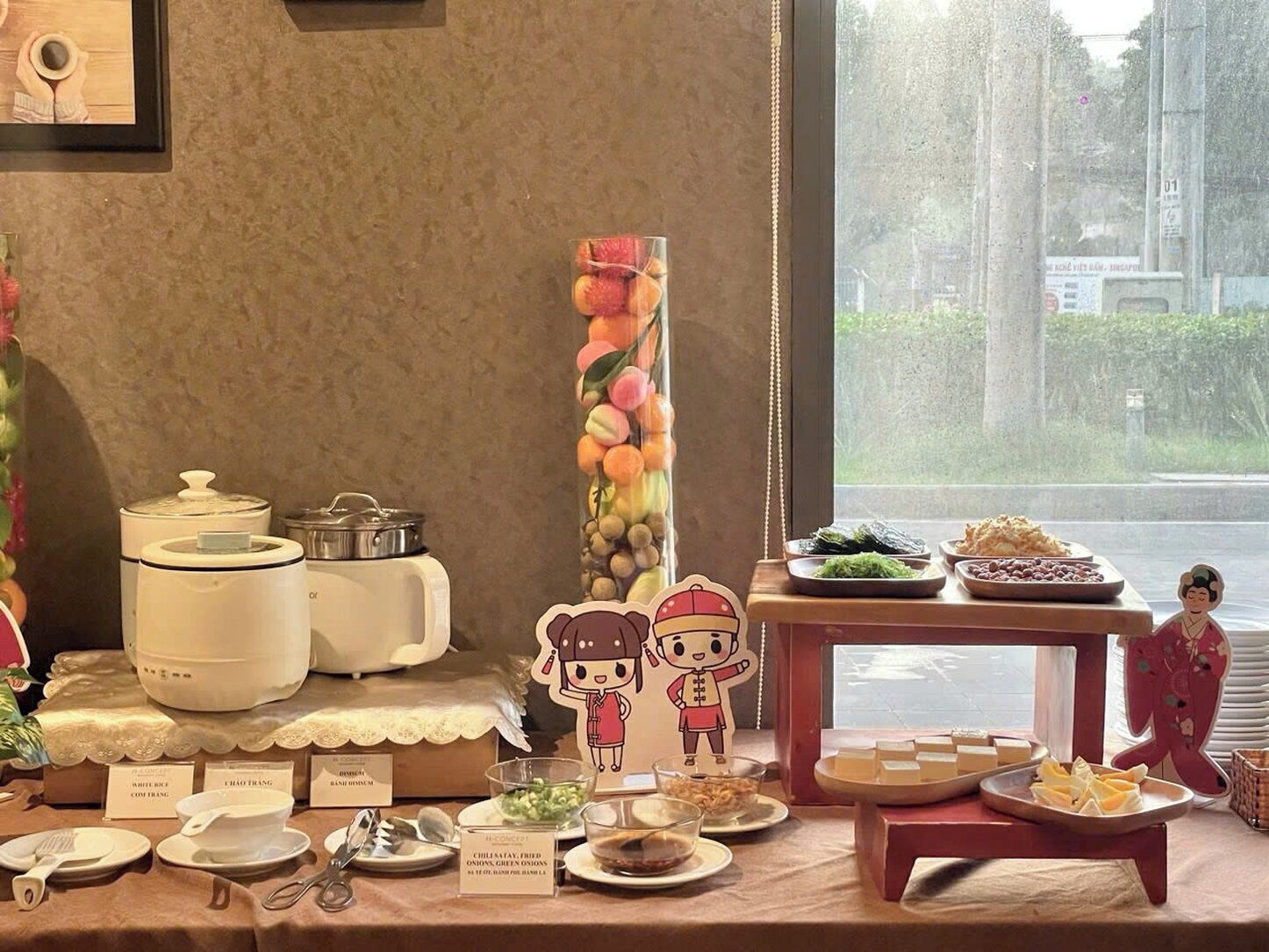 Une table dressée pour le petit-déjeuner, avec différents plats et un joli bocal rempli de fruits.