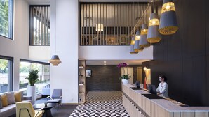 Un área de recepción moderna con mostrador de recepción, zona de estar con sofás y sillones, suelo con diseño y lámparas colgantes.