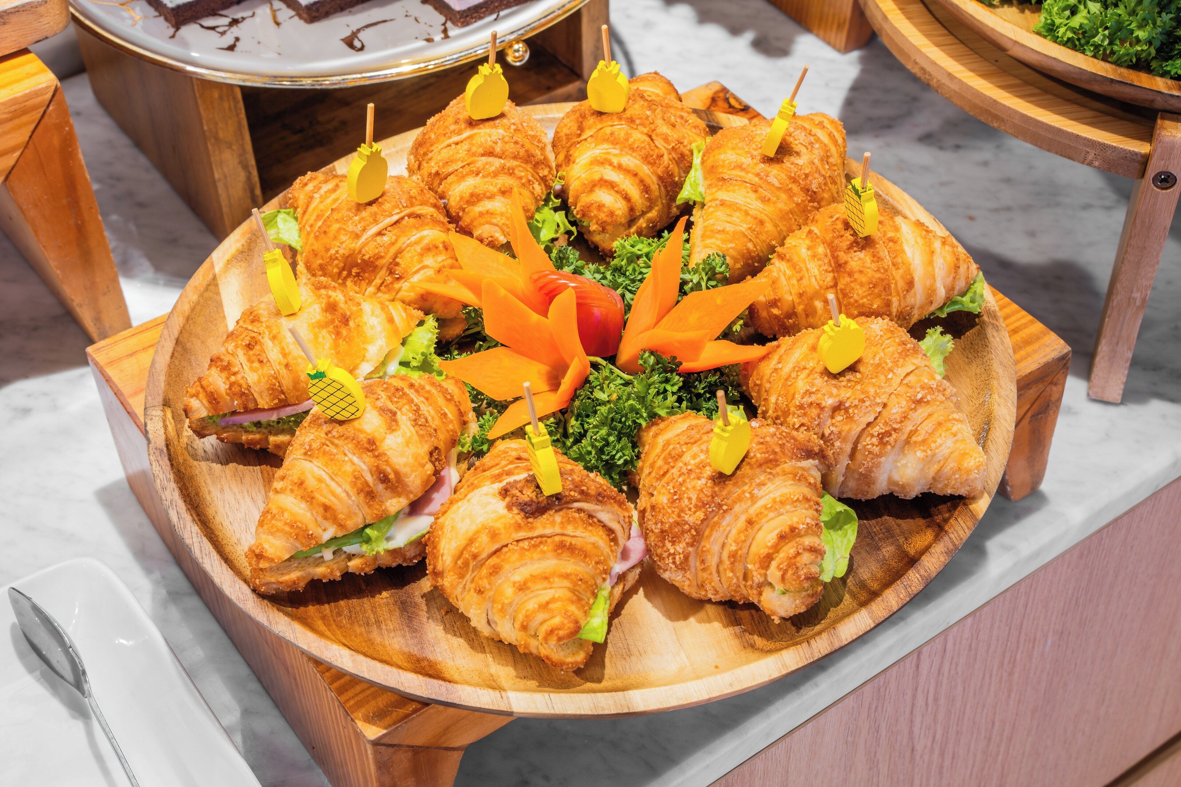 A wooden tray with croissants and vegetables on a marble countertop.