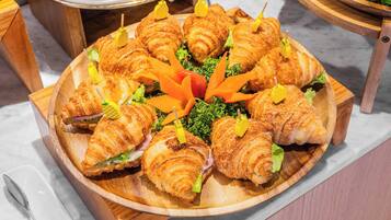 A wooden tray with croissants and vegetables on a marble countertop.