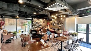 Un café moderno con mesas y sillas de madera, una barra de café y cuadros en las paredes.