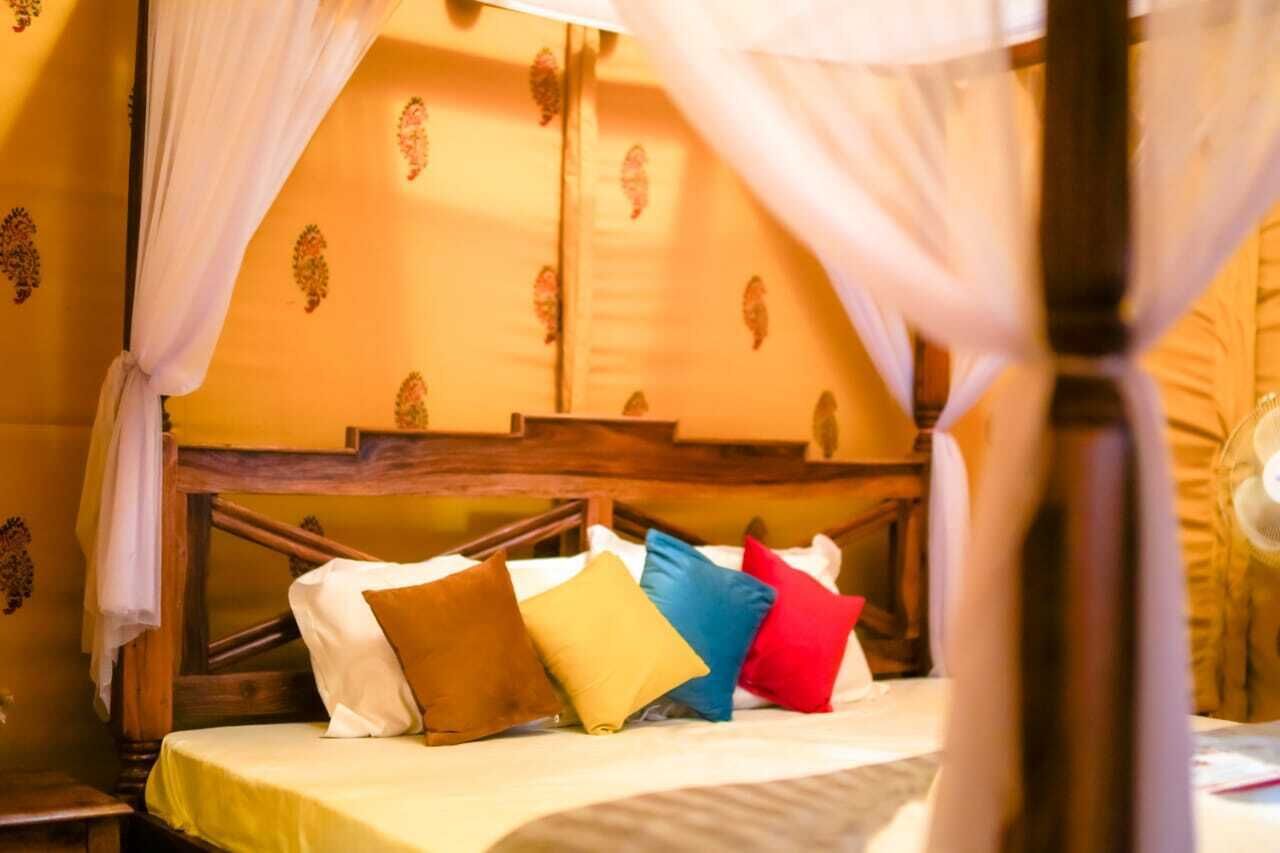 Un lit avec une tête de lit en bois, des oreillers blancs et bruns, et un baldaquin.