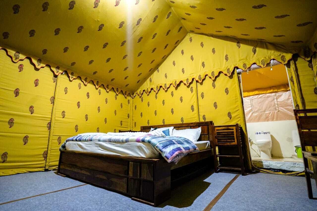 Een tentvormige kamer met een bed, houten hoofdbord en een klein tafeltje.