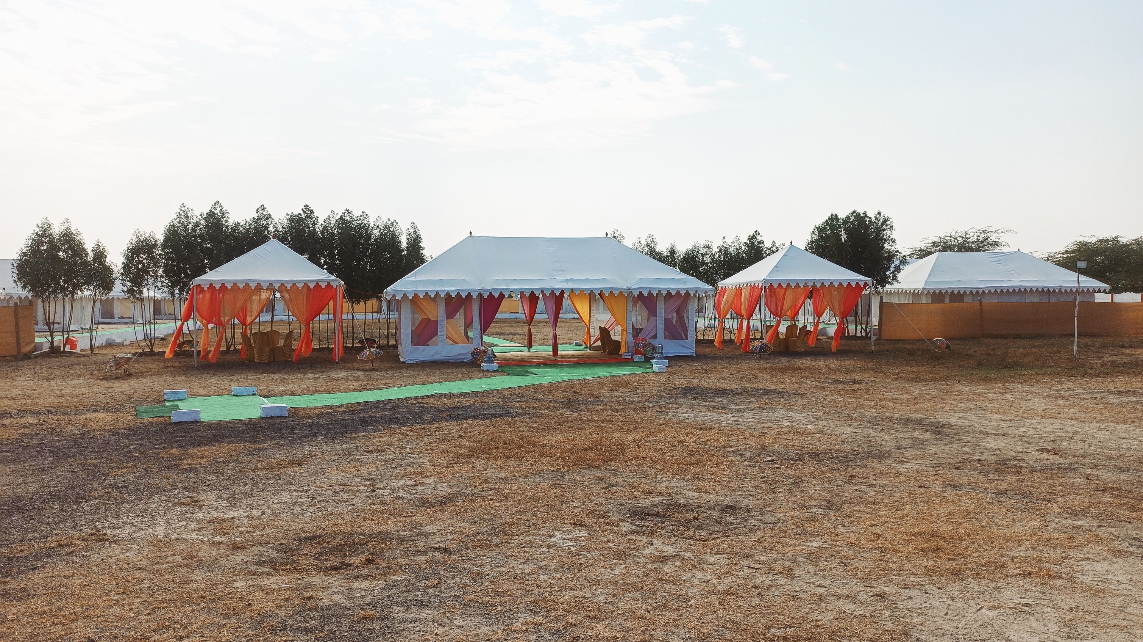A series of tents with a stage in the center, surrounded by chairs and tables, set up in an open field.