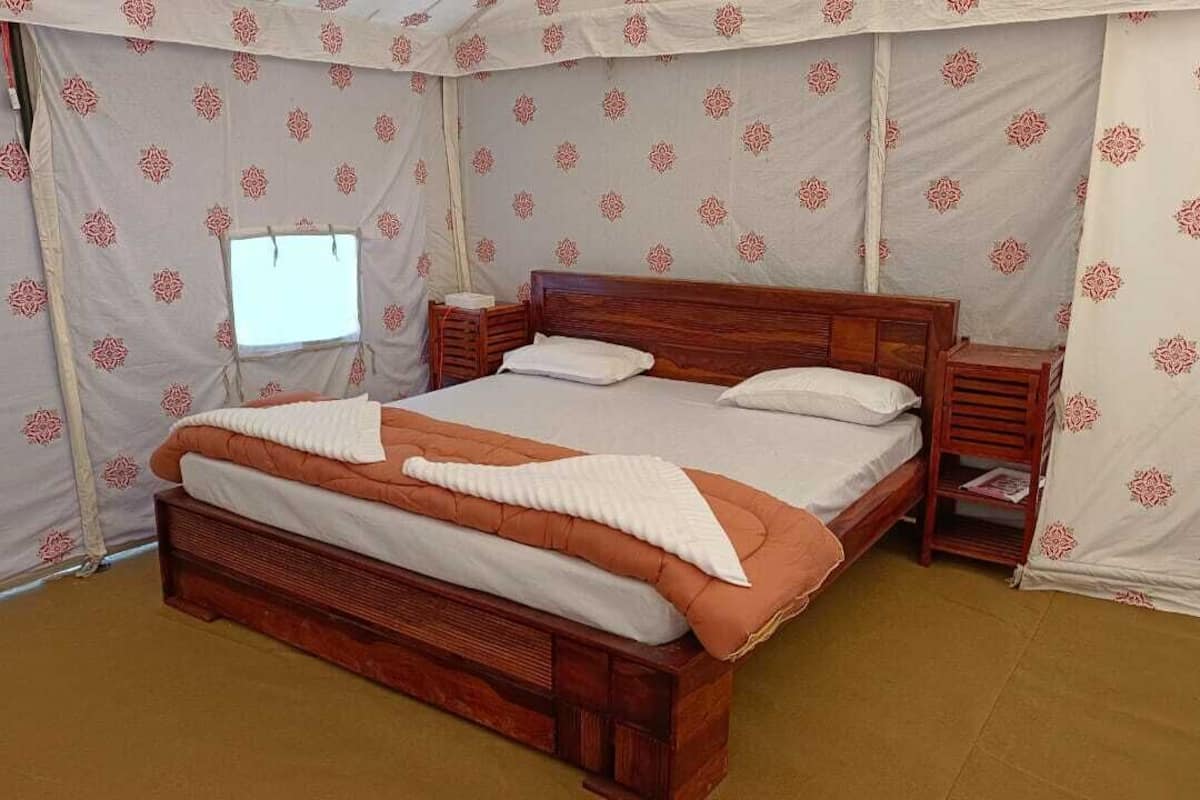 A single bed with a wooden frame and a white and orange bedspread in a tent-like room with patterned walls.
