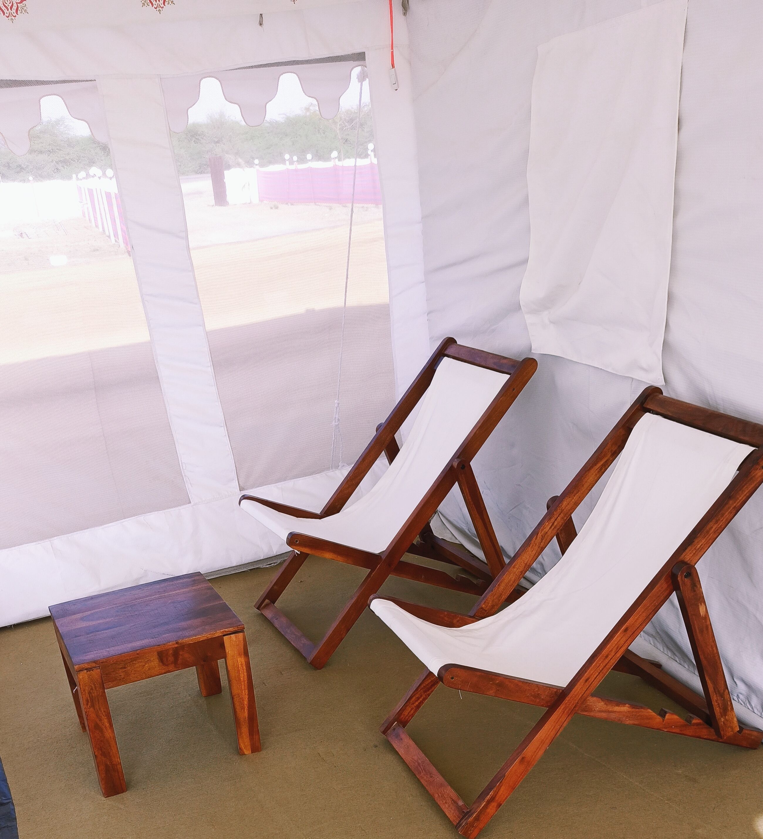 A tent with two wooden lounge chairs and a small table.
