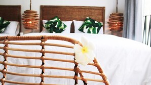 Un lit avec une literie blanche, une chaise en osier ornée d’une fleur blanche et une tête de lit avec un motif tissé.