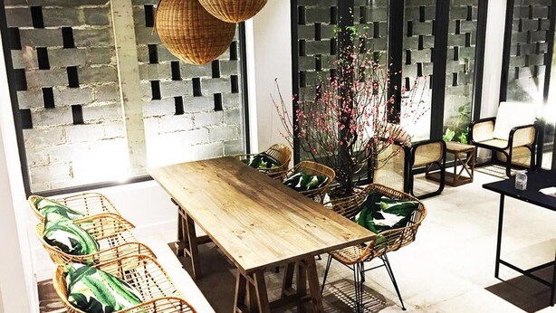 Un coin repas avec une table en bois et des chaises en osier, une plante en pot et un mur au motif de briques.