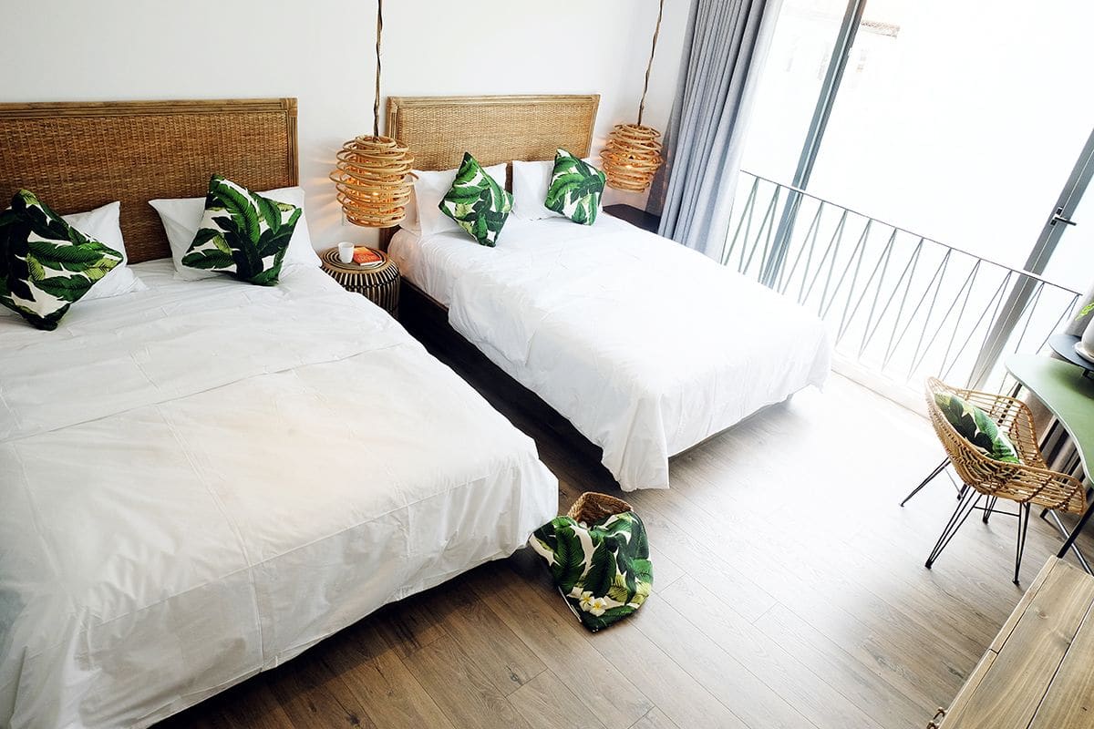A hotel room with two beds, wicker headboards, white bedding, and a wicker chair.