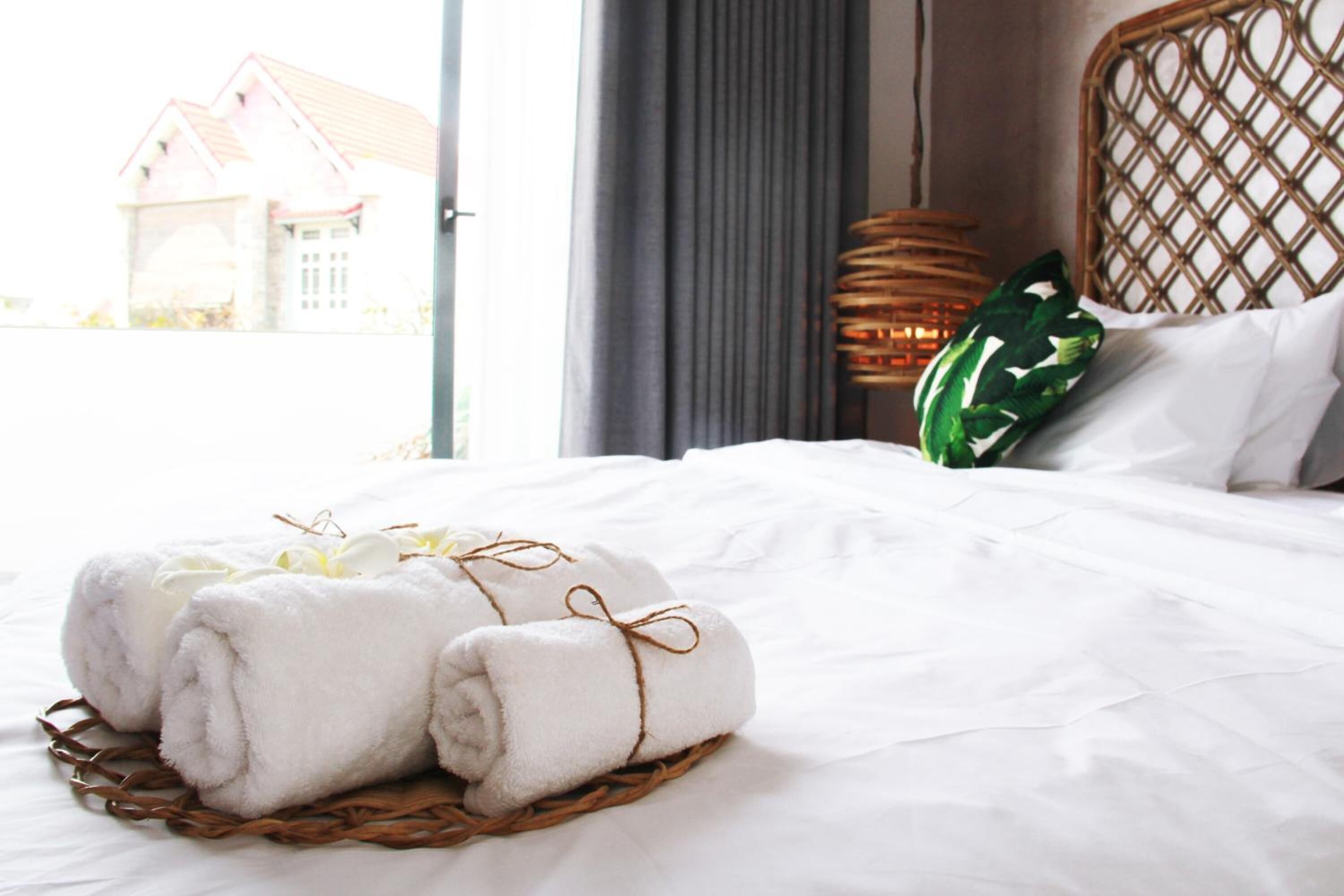 A neatly made bed with white linens and a basket of rolled towels tied with a brown string.