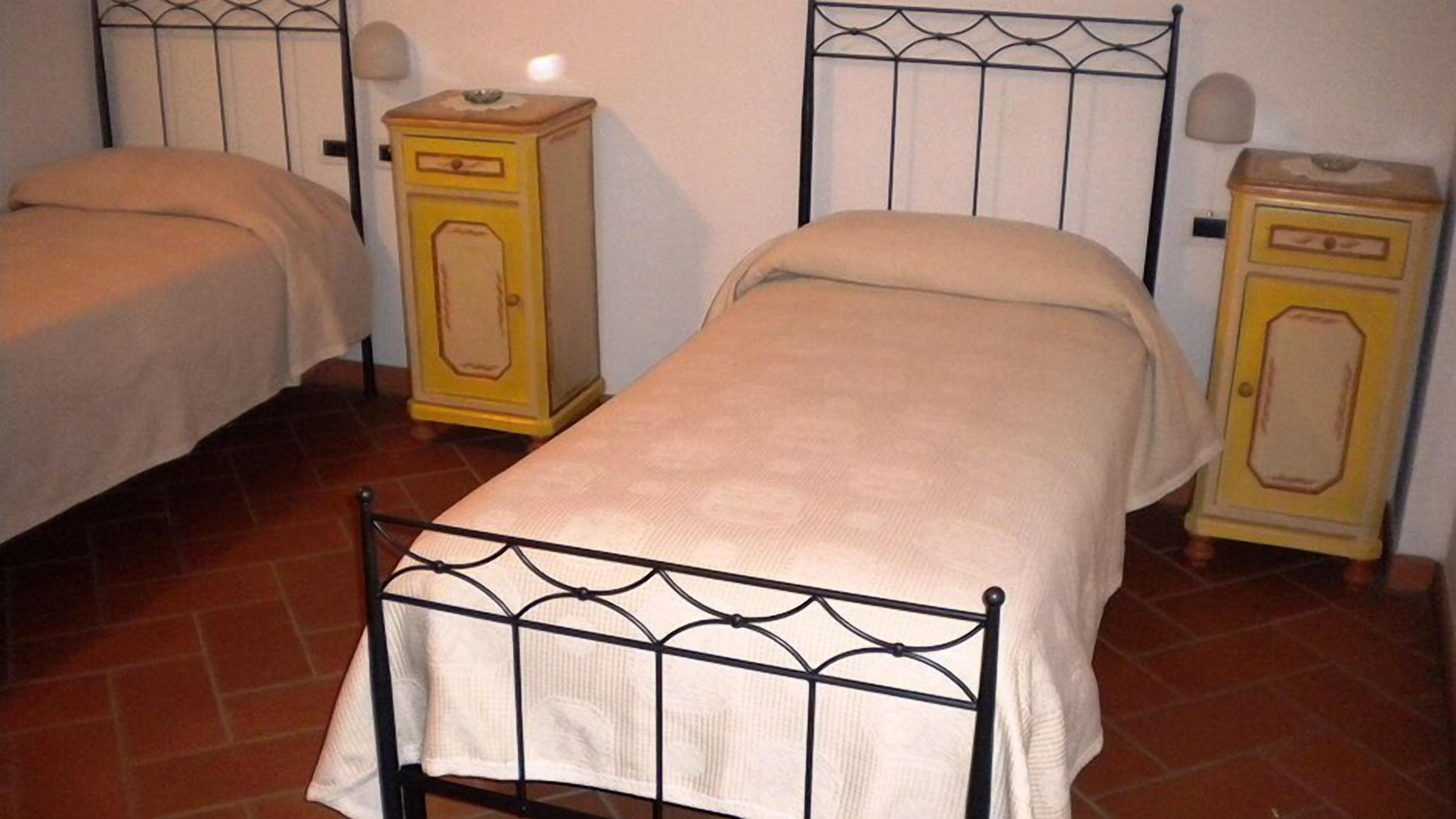 A single bed with a metal frame and a plain mattress, flanked by two small bedside tables with yellow cabinets.