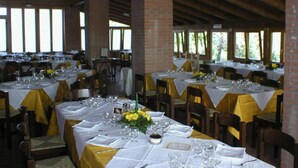 Une grande salle à manger avec de nombreuses tables dressées pour un repas, caractérisée par des murs en briques et de grandes fenêtres.