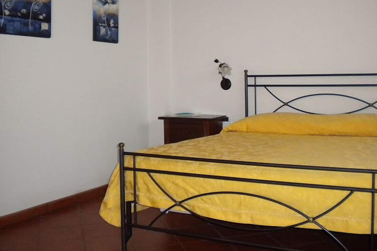 Un lit simple avec un cadre en métal et une couvre-lit jaune, dans une pièce aux murs blancs.
