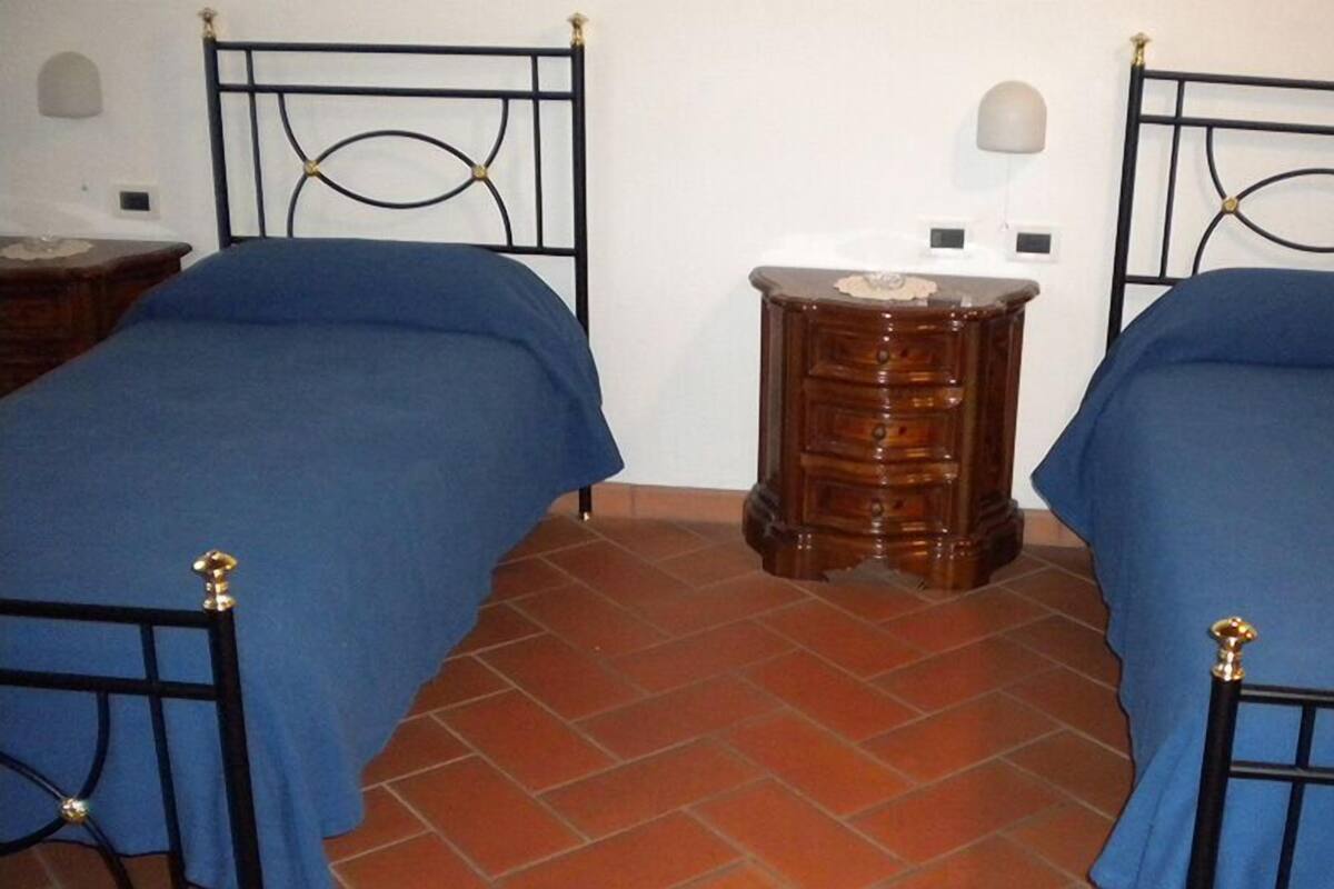 Une chambre avec deux lits, chacun recouvert d’une couvre-lit bleue et doté d’un cadre en métal noir, une table de chevet en bois avec des tiroirs et un sol carrelé.