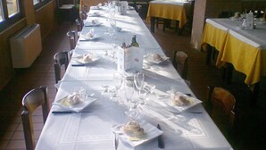 Une longue table à manger, dressée avec des nappes blanches, des assiettes, des verres et des couverts.